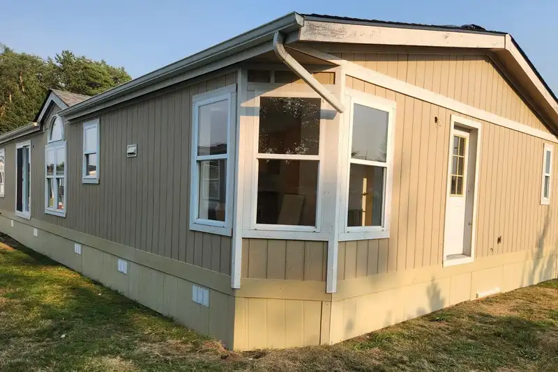 Manufactured home freshly painted tan with white trim, a white bay window and two-tone skirting