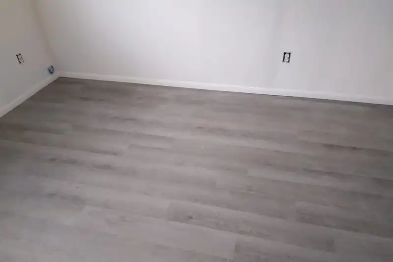 New gray vinyl plank floor with fresh white baseboard in an empty bedroom