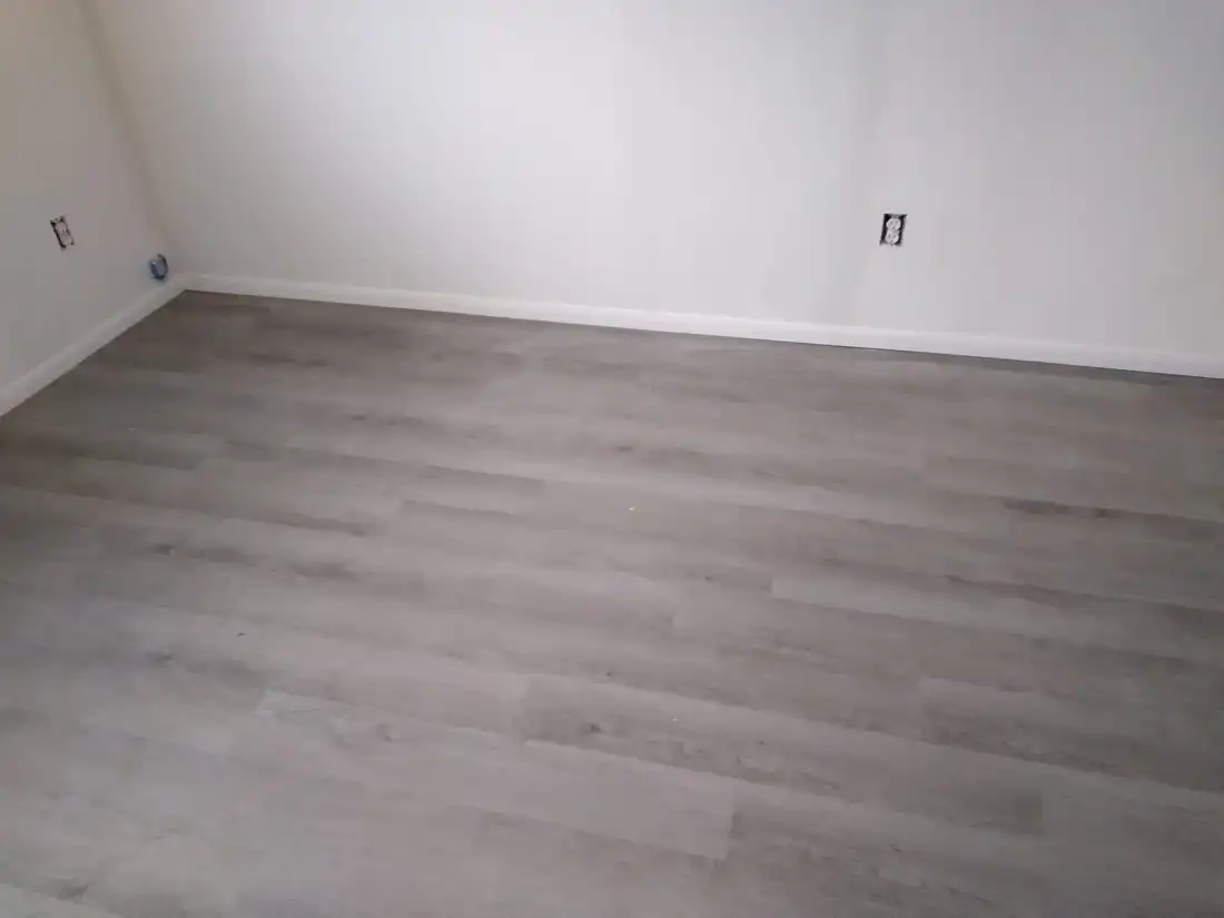 New gray vinyl plank floor with fresh white baseboard in an empty bedroom