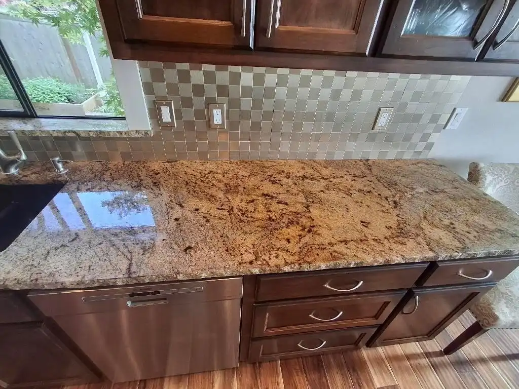 Polished granite kitchen countertop below dark wood cabinets and a metal tile backsplash, Camano Island
