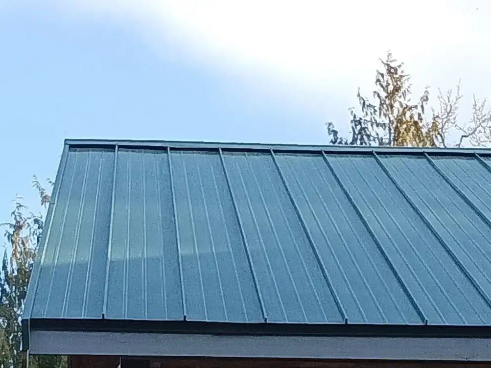 Green standing-seam metal roof at a gable end against a blue sky, Stanwood